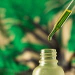 Dropping,Essential,Oil,Into,Glass,Bottle,On,Blurred,Green,Background.